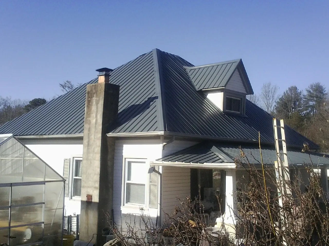 Dark blue standing seam metal roof on a white farmhouse with dormer — Slate & Tile Roof Repair by Roofing Brothers in The Colony