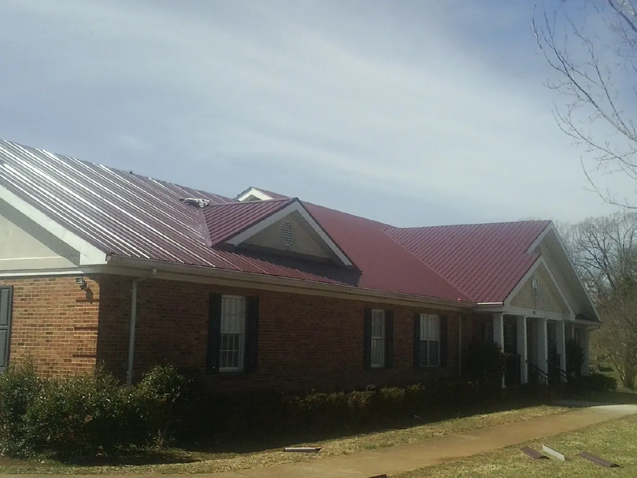 Red metal roof with gabled entries on a long brick building, from a Hail Damage Roof Repair job in The Colony