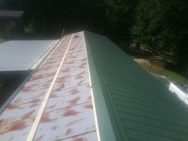 Old rusted panels beside newly installed green metal roofing — Wind Damage Roof Repair by Roofing Brothers in The Colony