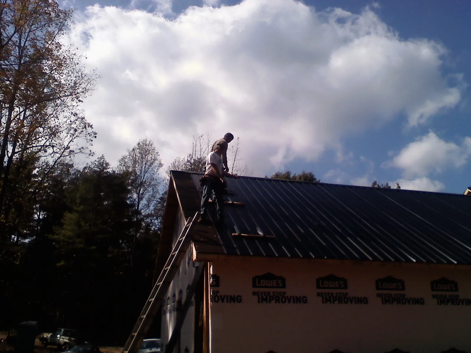 Roofer fastening dark metal panels high against a cloudy sky, from a Roof Inspection job in The Colony