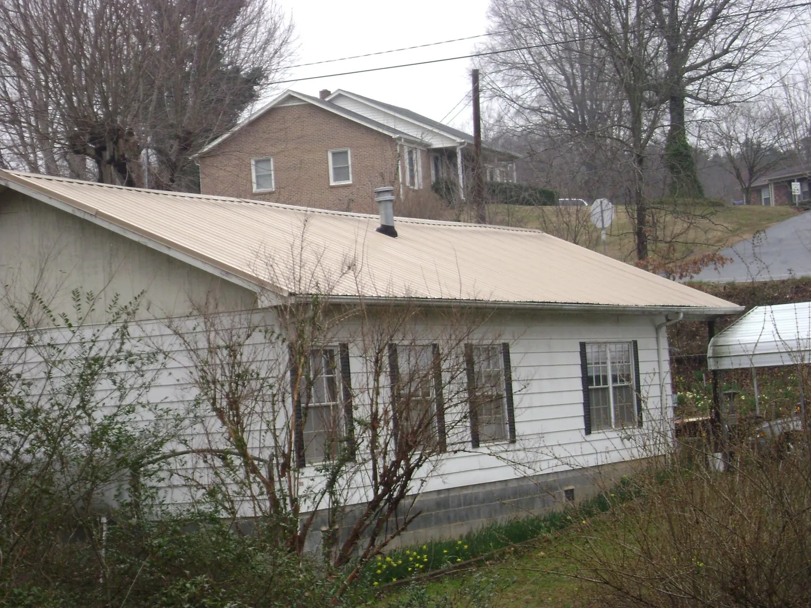 Tan metal roof on a white sided house set into a hillside — Commercial Roofing by Roofing Brothers in The Colony
